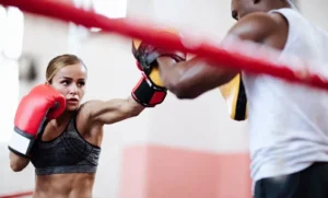 Amidst the state-of-the-art facilities of our prestigious boxing gym in Dubai, a dedicated woman unleashes her power with precision. Her red gloves connect sharply with the trainer's pads, expertly guided by her coach. Every punch refines her technique and brings her closer to mastery in the art of boxing, embodying the spirit and dedication we cultivate here.