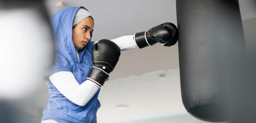 Within the walls of our elite boxing gym in Dubai, a dedicated and powerful woman embodies commitment and strength. Clad in a sleek blue hoodie and black boxing gloves, she delivers precise punches to the heavy bag. Her unwavering dedication to fitness remains steadfast, even as she gracefully observes Ramadan, showcasing the perfect blend of discipline and vitality that we nurture here.