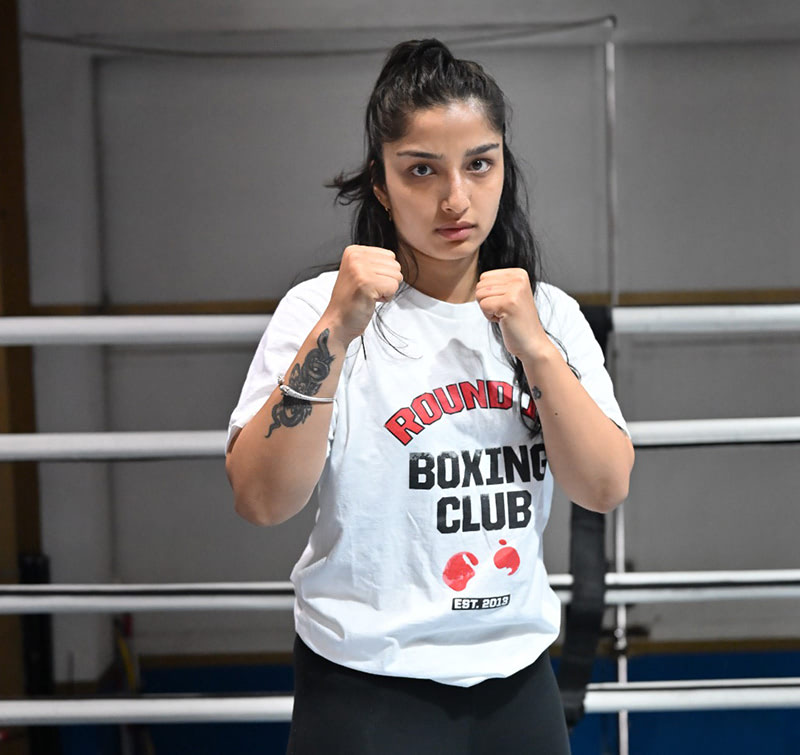 في صالة الألعاب الرياضية الرائدة لدينا في دبي، ترتدي امرأة بفخر قميص "Round Boxing Club"، وتقف في الحلبة وقبضتيها مرفوعتين للقتال.