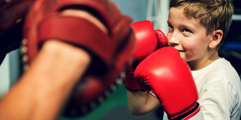 في صالة الملاكمة النخبوية لدينا في دبي، يقوم رياضي شاب يرتدي قفازات حمراء بصقل مهاراته مع مدرب يستخدم وسادات تركيز احترافية.