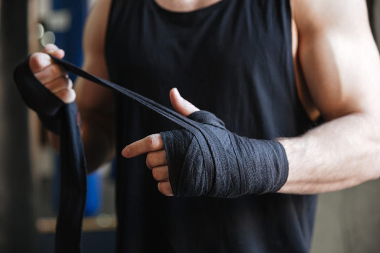 An athlete in a sleeveless black vest expertly wraps their hands, gearing up for elite training at a premier Dubai boxing facility.