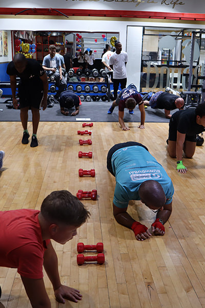 Members of our elite Dubai boxing gym are pushing their limits with intense plank exercises, lined up beside a striking array of red dumbbells on our pristine wooden floors.