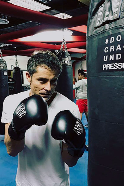 A dedicated fighter, donned in a crisp white T-shirt and sleek black boxing gloves, hones his craft amidst the elite setting of our established Dubai gym. Surrounded by top-tier punching bags, his movements echo precision and power, embodying the spirit of excellence that defines our specialized training environment.