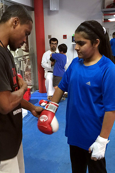 In the heart of Dubai’s premier boxing facility, an experienced coach imparts the art and discipline of boxing to a promising young athlete. Clad in a blue shirt and sporting quality boxing gloves, the young contender is guided through precision training techniques amidst state-of-the-art equipment. Here, in this exclusive setting, each jab and punch is crafted under expert supervision to inspire excellence and ignite potential.