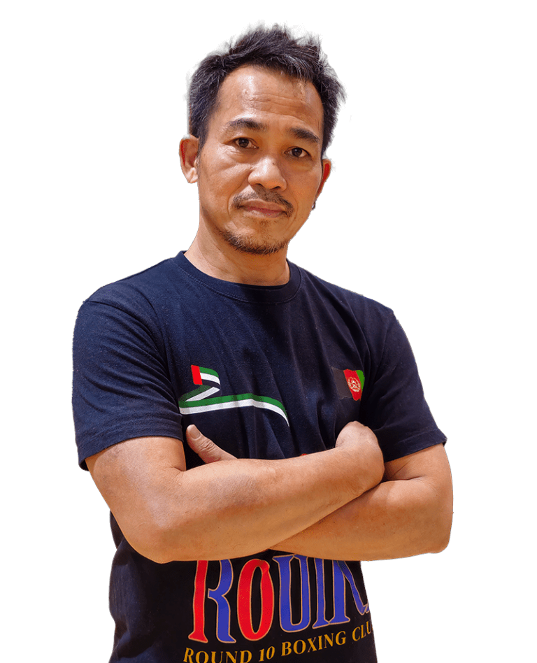 A confident man with arms crossed in a "Round 10 Boxing Club" tee stands before a white backdrop, ready for Dubai's boxing elite.