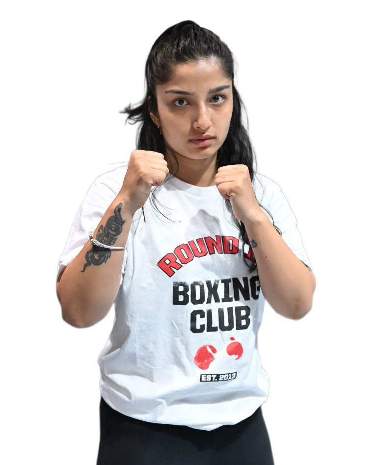 A focused woman in a "Round 1 Boxing Club" tee and black pants strikes a boxing pose at our elite Al Quoz gym, facing the camera.